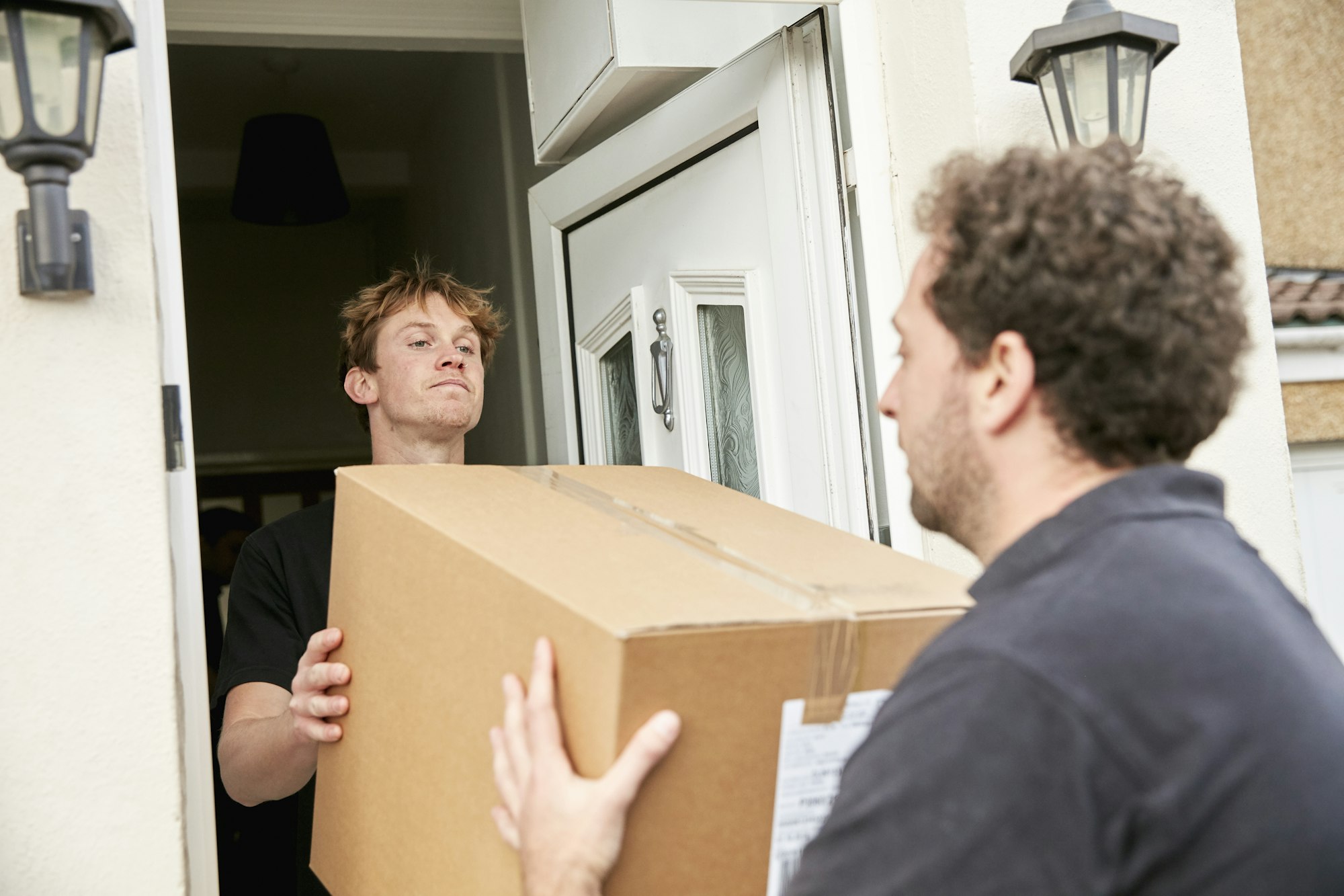 Removals business. Two men lifting and carrying a packed box out of a house.