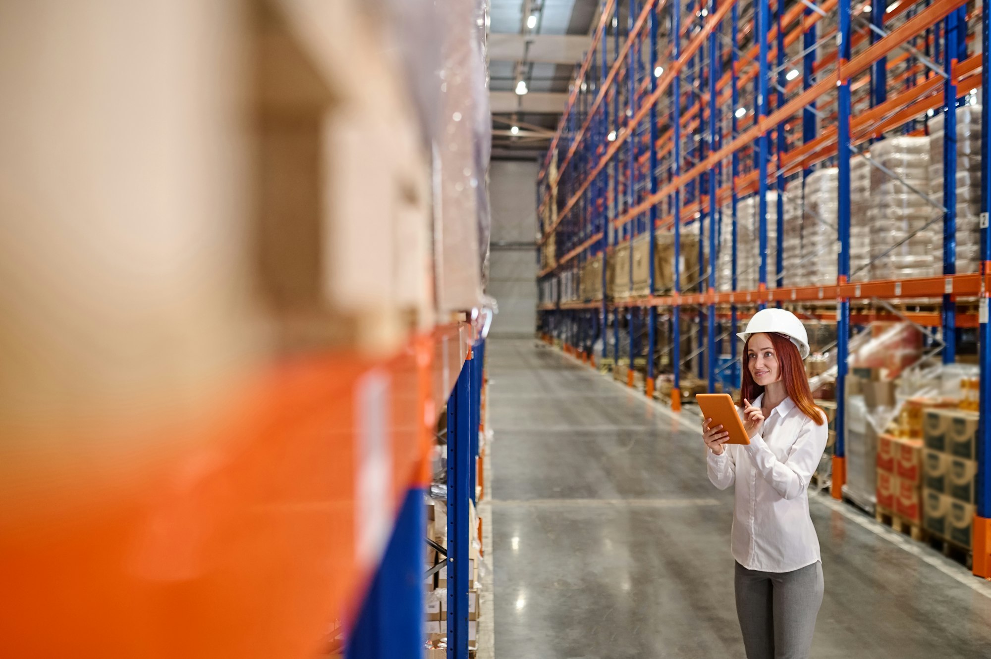 Woman with tablet looking at cargo in warehouse